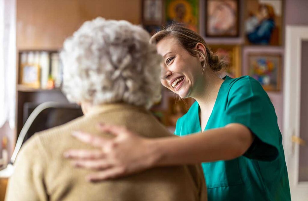 A senior resident sits in a cozy room with family members holding hands and sharing a quiet, supportive moment.