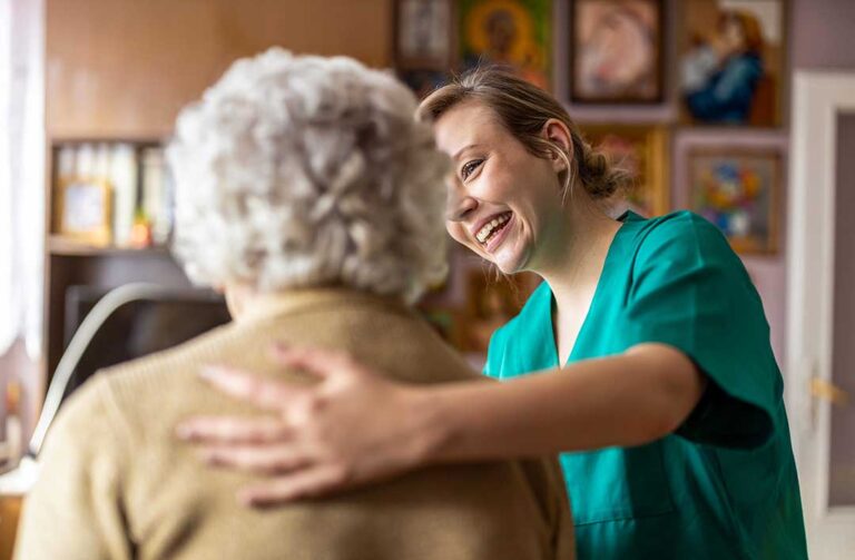 A senior resident sits in a cozy room with family members holding hands and sharing a quiet, supportive moment.